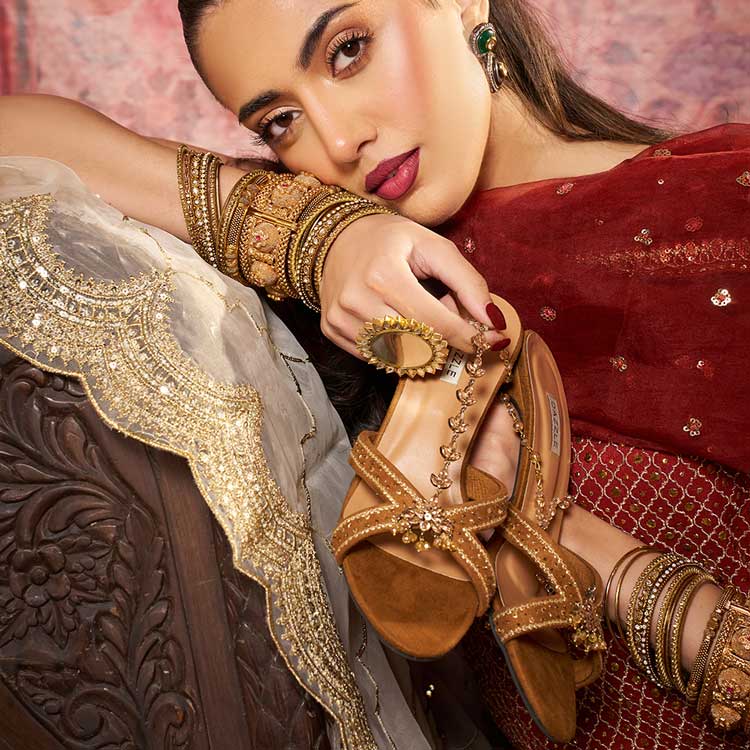Woman in traditional attire holding embellished tan sandals, wearing gold bangles and ring