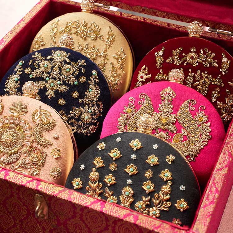 Handcrafted embroidered clutches with gold threadwork in a decorative box, traditional Pakistani accessories.